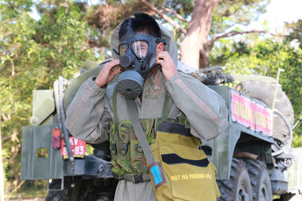 Binh nhất Y Quynh Kpơh trong bộ quần áo phòng hóa và chiếc mặt nạ phòng độc đặc chủng.